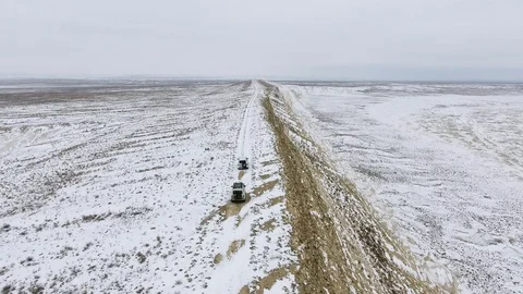 Three SUVs moving along the edge of a sandy cliff of the snow-covered desert in Stock Footage 93996876