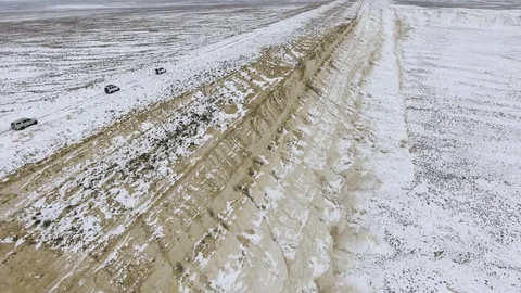 Three SUVs moving along the edge of a sandy cliff of the snow-covered desert in Stock Footage 93997242