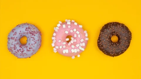 Three sweet donuts moving right and left on yellow background. Stop motion Stock Footage 128922611