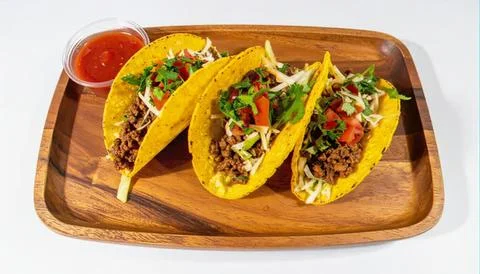 Three tacos with ground beef, vegetables, and salsa on wooden tray Stock Photos