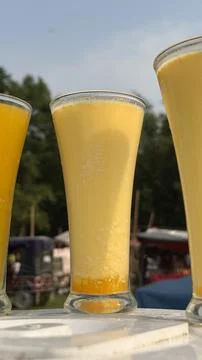 Three tall glasses filled with a vibrant yellow mango lassi, a traditional In 스톡 사진
