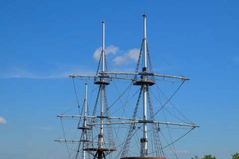 Three tall ship masts stand against a clear blue sky. Metal rigging stretches Stock Photos