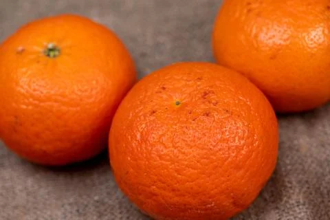Three tangerines on a table covered with a homespun cloth with a rough texture Stock Photos