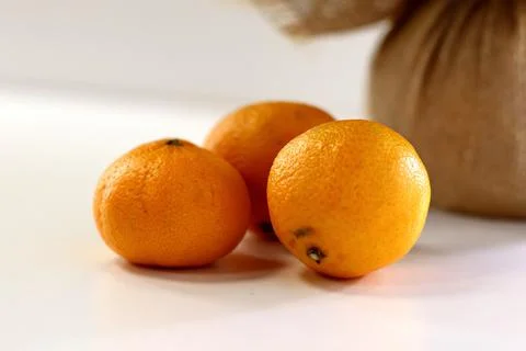 Three tangerines on a white table and a brown bag behind Stock Photos