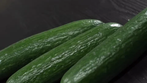 Three tasty green cucumbers rotating on black wooden table close up view from 스톡 동영상 148165757