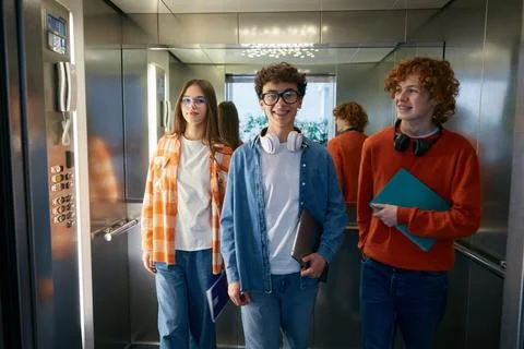 Three teenagers standing inside the elevator holding folder with papers Stock Photos