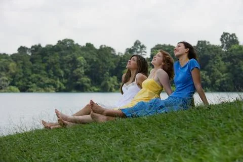 Three teens sitting on grass next to lake Stock Photos