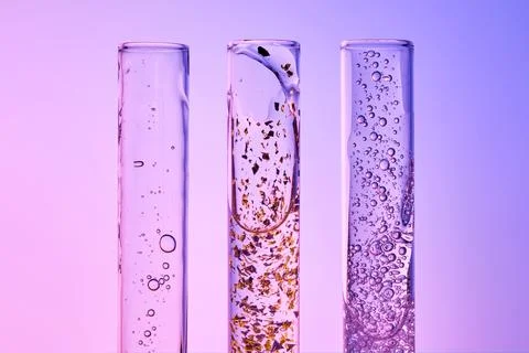 Three test tubes with different serums on a gray-purple background. Stock Photos