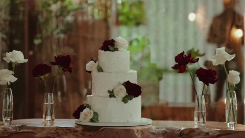 Three Tier White Wedding Cake with Red and White Roses on a Wooden Table Stock Footage 338437292