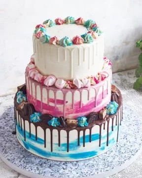 Three-tiered colored cake with colored smudges of chocolate on a light backgr Stock Photos