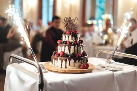 Three-tiered wedding cake with dripped chocolate and berries standing on serving Stock Photos