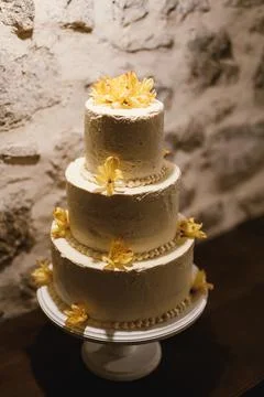 Three-tiered wedding cake on a rotating stand against a white stone wall 스톡 사진