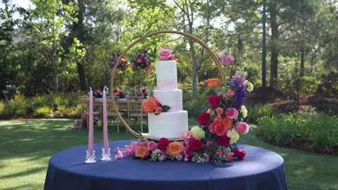 Three-tiered wedding cake standing in round arch with bouquet on table outdoors Stock Footage 249777241