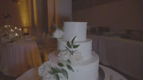 Three-tiered white wedding cake decorated with white roses and greenery Stock Footage 174765160