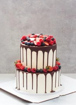 A three-tiered white wedding cake decorated with fresh bright berries and mel Stock Photos