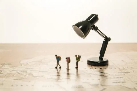 Three tiny human models walk on world map with lamp Stock-Fotos