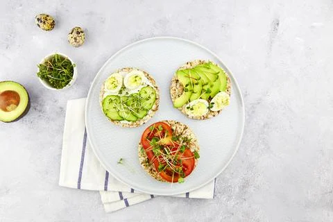 Three toasts with egg, avocado, micro greens, cucumbers and tomatoes. Stock Photos