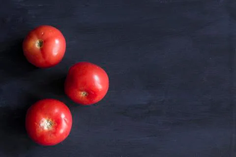 Three tomatoes in a dark blue table Stock Photos