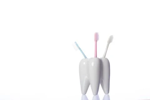 Three toothbrushes in ceramic tooth-shaped stand isolated on white background Stock Photos