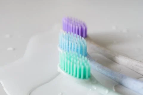 Three toothbrushes of different colors on white background. Stock Photos