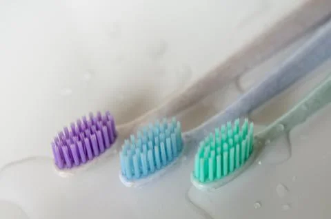 Three toothbrushes of different colors on white background. Stock Photos