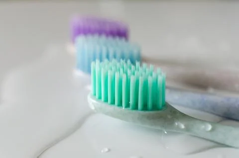 Three toothbrushes of different colors on white background. Stock Photos