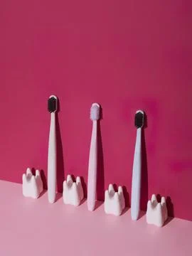 Three toothbrushes standing with small toothpaste models on pink background Fotos Stock