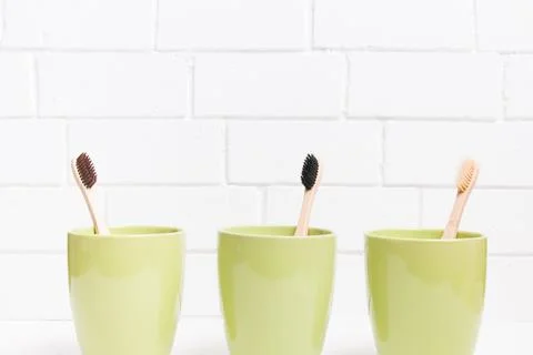 Three toothbrushes in three different green cups on a white background, bambo Stock Photos