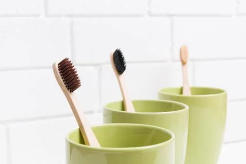 Three toothbrushes in three different green cups on a white background, bambo Stock Photos