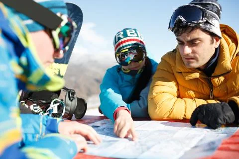 Three tourists explore map in winter resort. Stock Photos