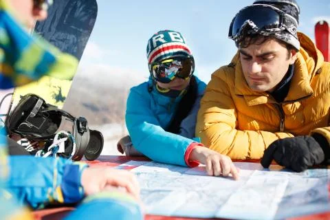 Three tourists in mask explore map in winter resort. Stock Photos