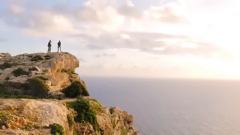 Three tourists stand on the edge of a cliff at a great height and look at the Video stock 101536340
