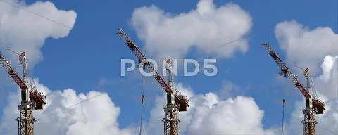 Three tower cranes on a background of blue sky and white clouds Stock Illustration