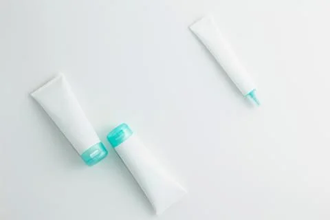 Three turquoise and white cosmetic tube mockups on white background. Flat lay. Stock Photos