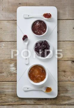 Three types of jam in bowls with spoons on a board Stock-Fotos