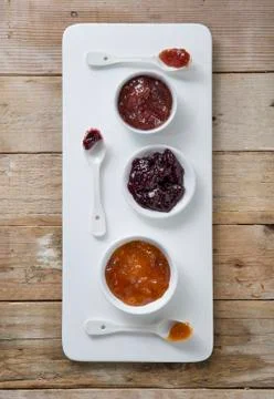Three types of jam in bowls with spoons on a board Stock Photos