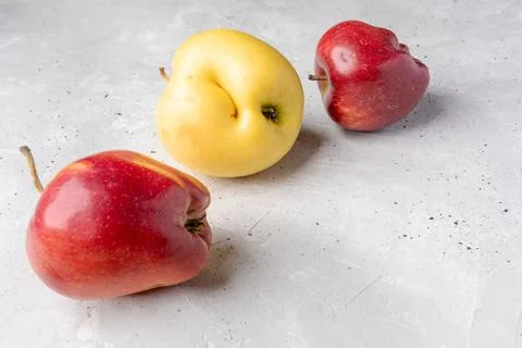 Three ugly red and yellow apples are lying chaotically on grey concrete bac.. Stock Photos