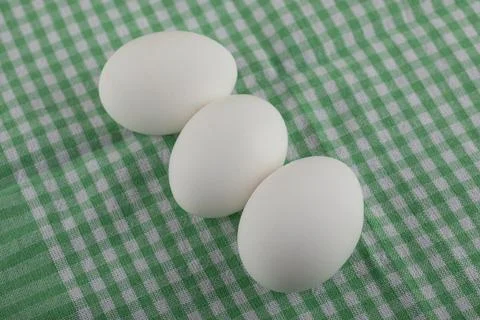Three uncooked eggs on striped tablecloth Stock Photos