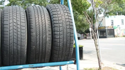 Three used tires side by side on blue rack outside exterior on bright days Stock Footage 252043725
