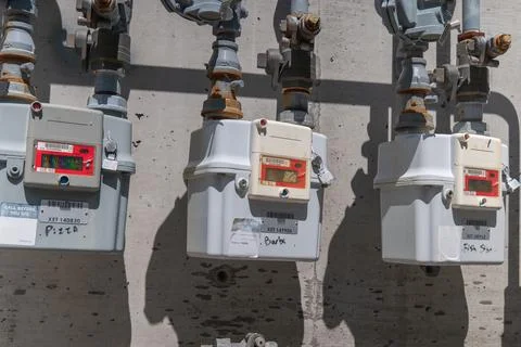 Three utility meters attached to a concrete wall show labels and pipes Foto stock