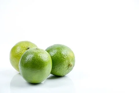 Three vibrant green limes arranged on a clean white reflective surface Stock Photos