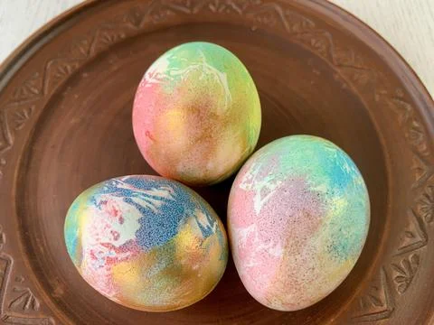 Three vibrant, hand-dyed Easter eggs sit on a rustic brown plate. Their colors Stock Photos