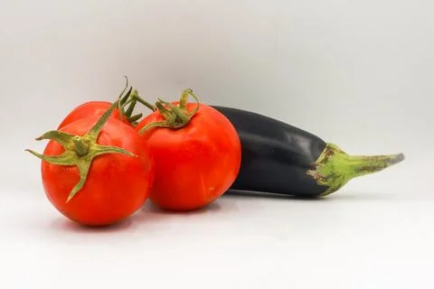 Three vine-ripened red tomatoes arranged in front of a single glossy purple Stock Photos