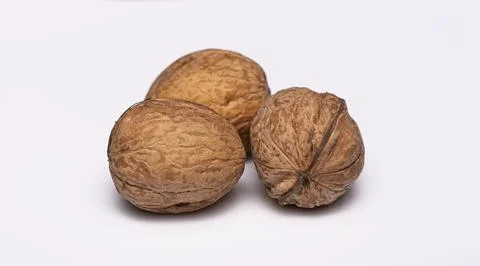 Three walnuts rest on a white surface Stock Photos