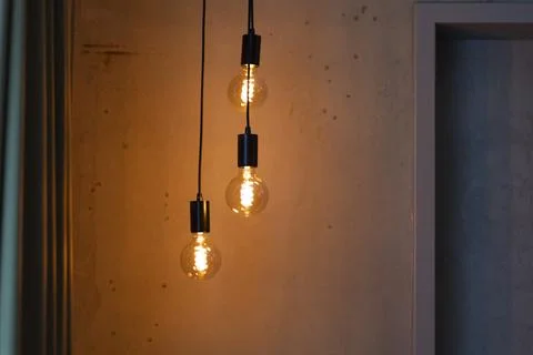 Three warm light bulbs hang from black cables, illuminating a textured wall i 写真素材