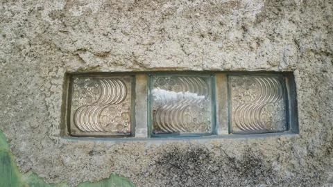 Three wavy glass blocks set in a rough unpainted concrete wall Stock Photos