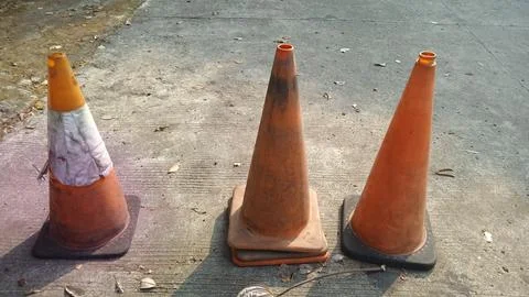Three weathered orange traffic cones on concrete pavement under bright morn.. Fotos de archivo