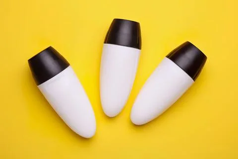 Three white and black deodorant bottles on yellow background Stock Photos
