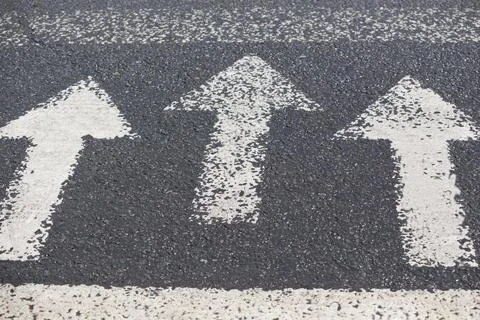 Three white arrows pointing in one direction on gray asphalt floor. Stock Photos
