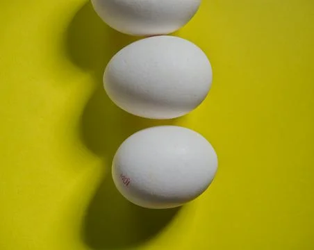 Three white bio eggs on yellow background, topview Stock Photos